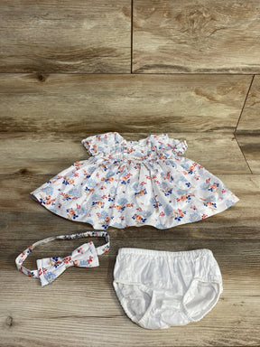 Overhead view of white floral pintuck baby dress set showcasing pintuck bodice and ruffled sleeves with matching headband and white bloomers on wood background
