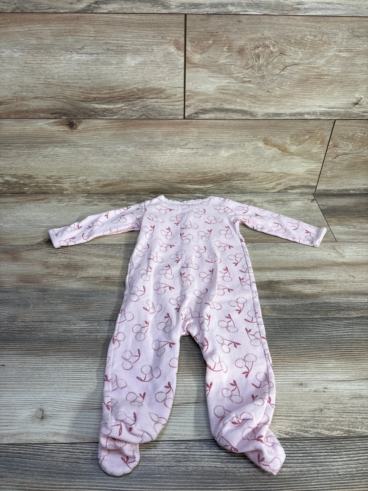 Flat lay of Just One You pink waffle knit footed sleeper with all-over cherry print and zip front on wood plank floor