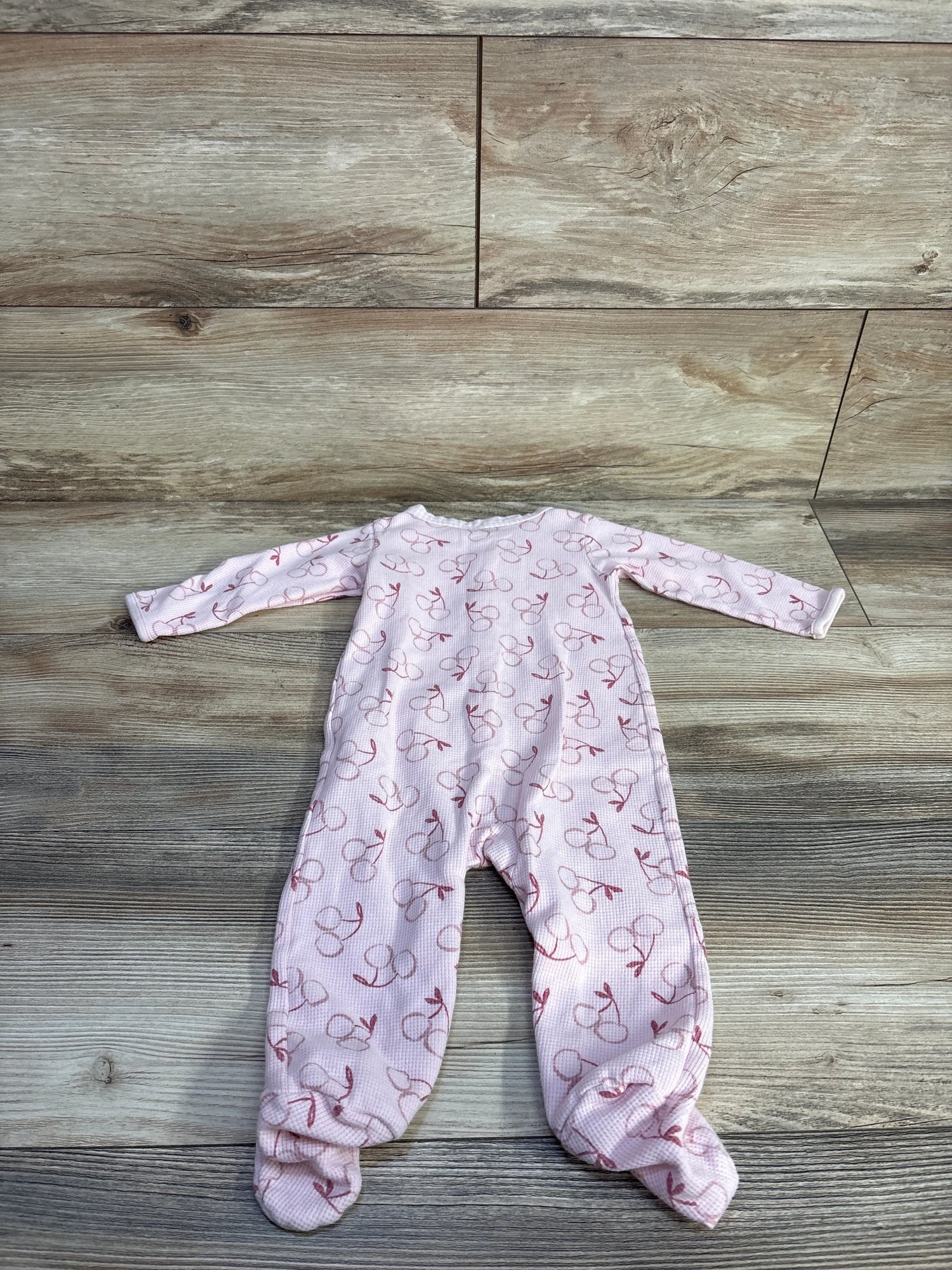 Flat lay of Just One You pink waffle knit footed sleeper with all-over cherry print and zip front on wood plank floor