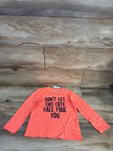 Long sleeve orange kids shirt with 'Don't let this cute face fool you' text, laid on wood floor