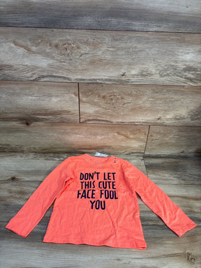 Long sleeve orange kids shirt with 'Don't let this cute face fool you' text, laid on wood floor
