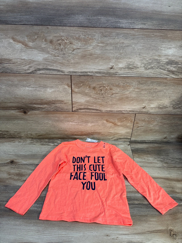 Long sleeve orange kids shirt with 'Don't let this cute face fool you' text, laid on wood floor