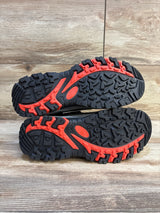 Black and red kids' athletic shoe soles with rugged tread on wood background