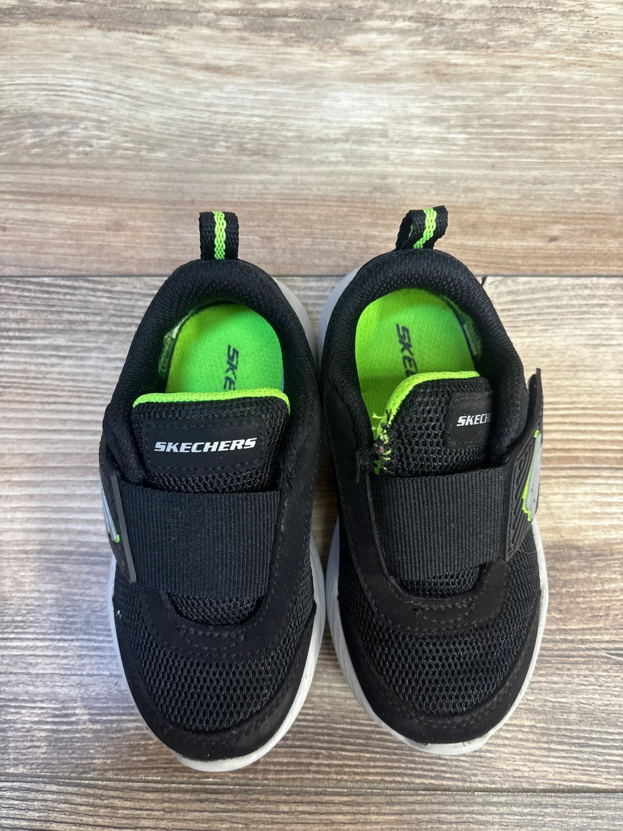 Black and green Skechers kids sneakers with Velcro straps on wood floor