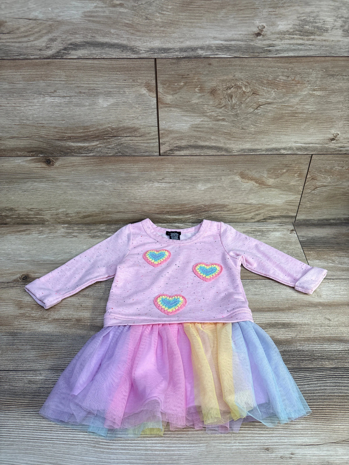 Front view of pink Zunie sweatshirt tulle dress showcasing long sleeves, heart embellishments, and rainbow tulle skirt on wood floor