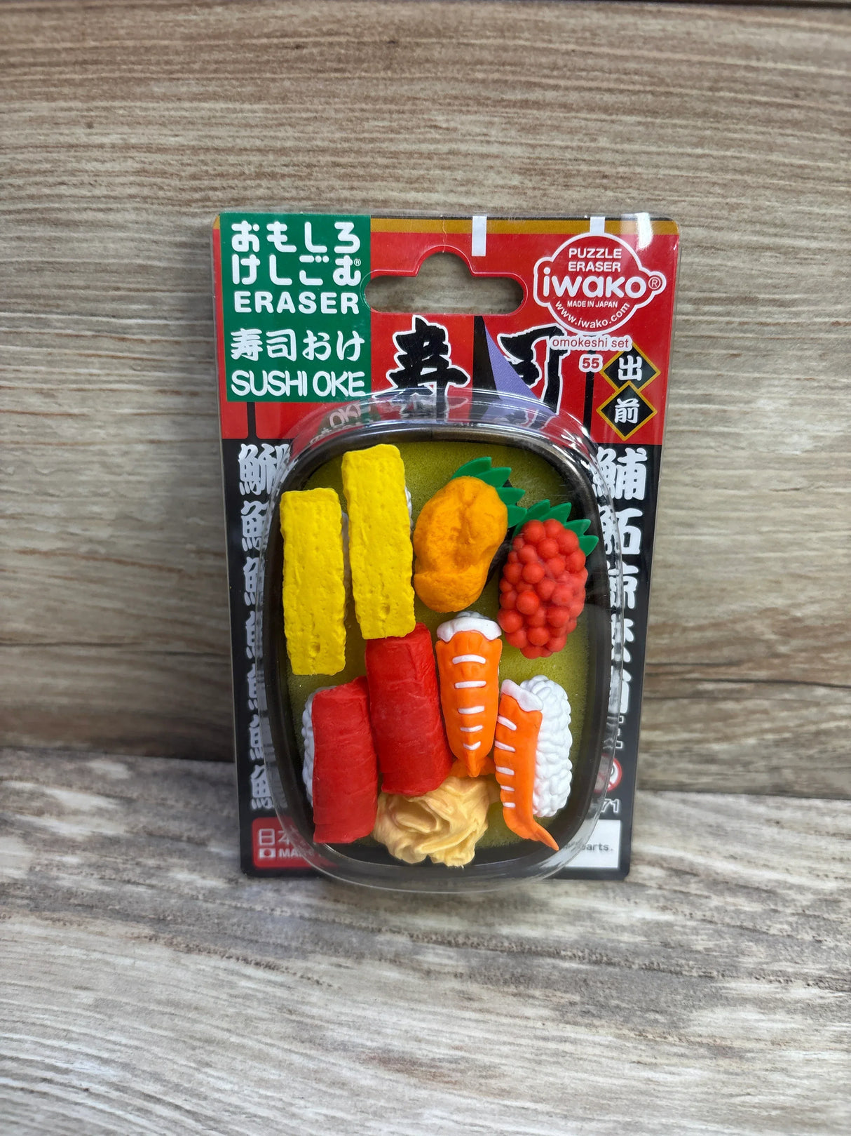 Front view of Iwako sushi eraser set with assorted sushi erasers (tamago, tuna, shrimp, roe) in blister pack on wood background