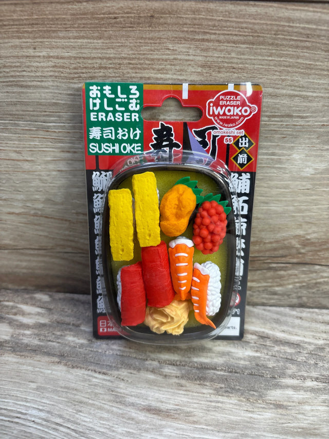 Front view of Iwako sushi eraser set with assorted sushi erasers (tamago, tuna, shrimp, roe) in blister pack on wood background
