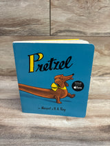 Front view of Pretzel board book with blue cover, illustrated dog in yellow bow tie, on a wood-grain background