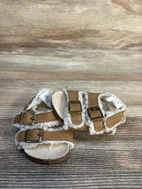 Tan toddler sandals with faux shearling lining and buckle straps on wooden background