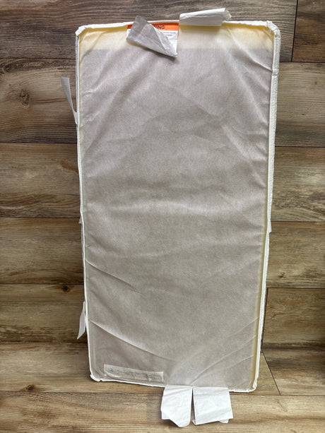 Back view of Serta Foam Contoured Changing Pad showcasing its light-colored fabric cover and side straps on a wood floor