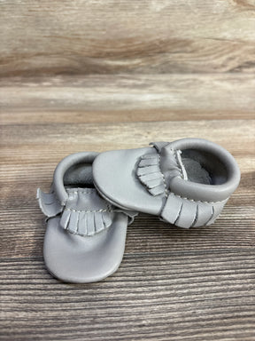 Pair of gray leather baby moccasins with fringe detail on wooden surface