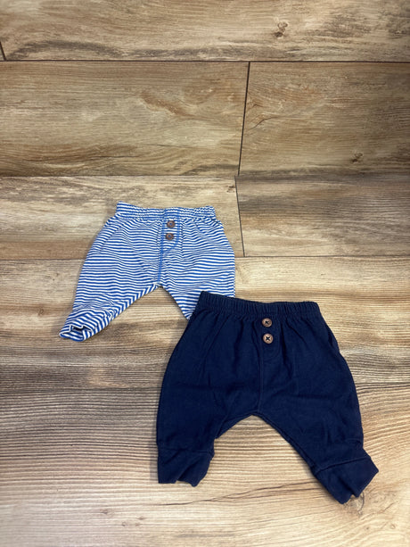 Top view of two-pack newborn pants showcasing blue and white stripes, navy fabric, and button closures with a wood floor background