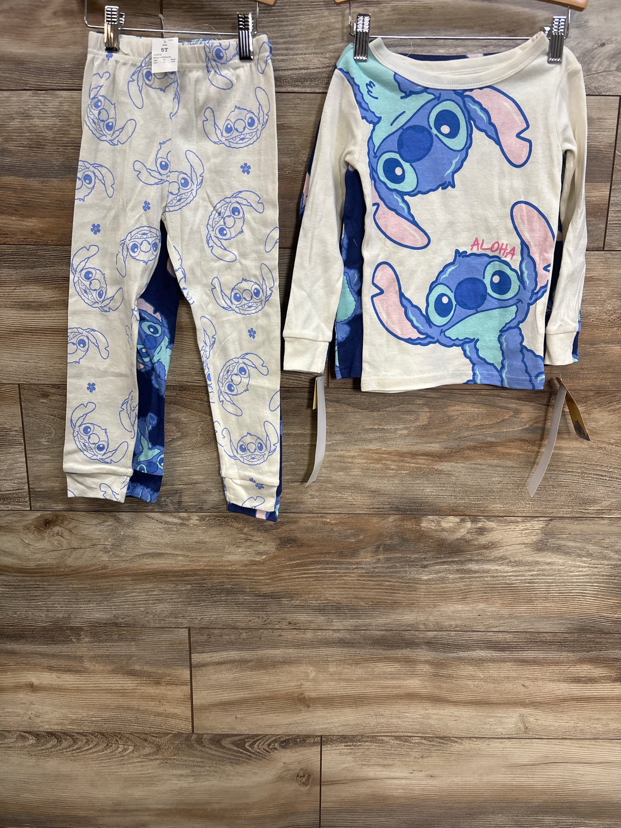 Front of blue Disney Stitch 4-piece pajama set size 5T showing top with large Stitch graphic and matching pants on wood wall
