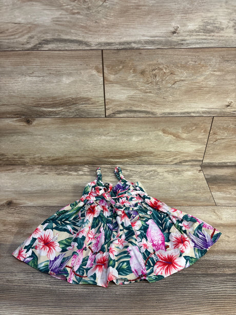Flat lay of baby sleeveless dress showcasing tropical floral and pink parrot print with braided straps on light wood background