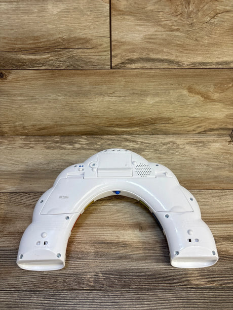 Back of Baby Einstein Glow and Discover Light Bar, curved white housing with battery compartment and speaker on wood floor
