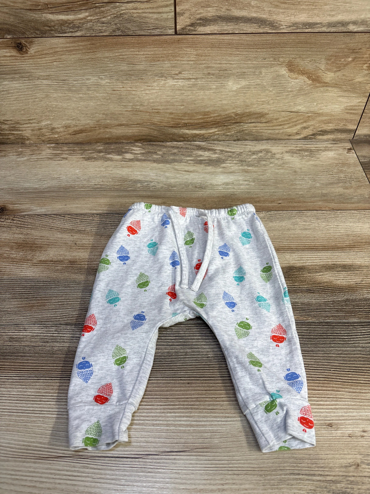Front flat-lay of grey baby harem pants (3-6M) with elastic waist, cuffed ankles and acorn print on wood