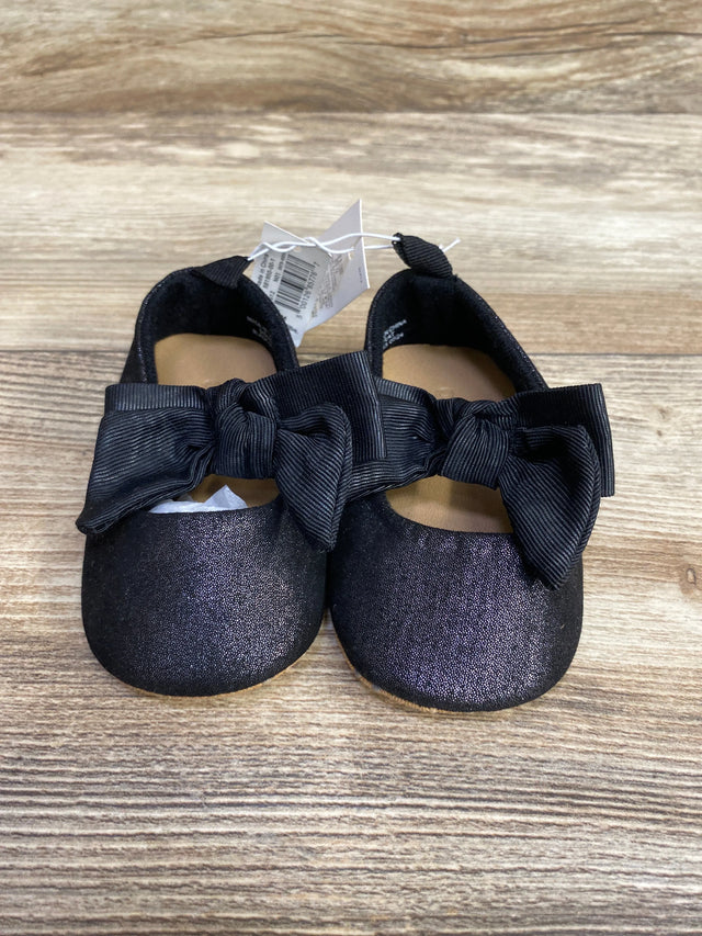 Pair of black baby shoes with large black bows on wooden surface, children's resale store item