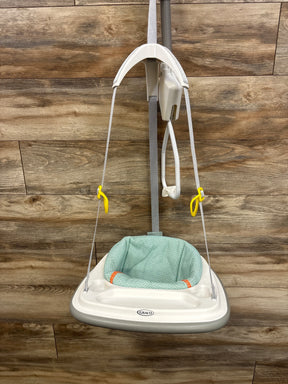 Graco baby swing with mint green seat, yellow hooks, and white frame against wood paneling