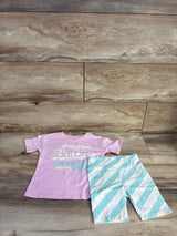 Flat lay of pink Malibu Barbie short-sleeve top and mint-and-white diagonal striped bike shorts on wood background