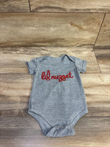 Flat lay of grey Sprout Joy Lil Nugget baby bodysuit showcasing red lil nugget chest print on wood plank background