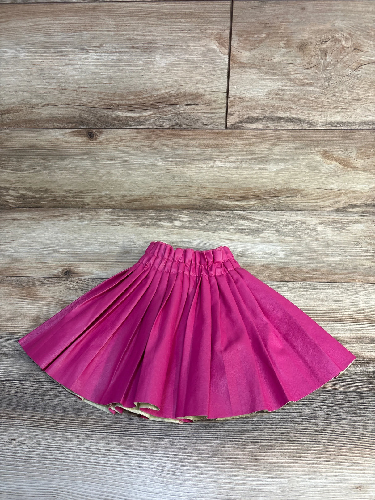 Bright pink pleated kids skirt with gold trim, laid flat on wood floor