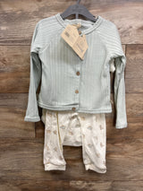 Front view of baby outfit on hanger showcasing light green ribbed cardigan with wood buttons and cream pants with animal print on wood plank floor