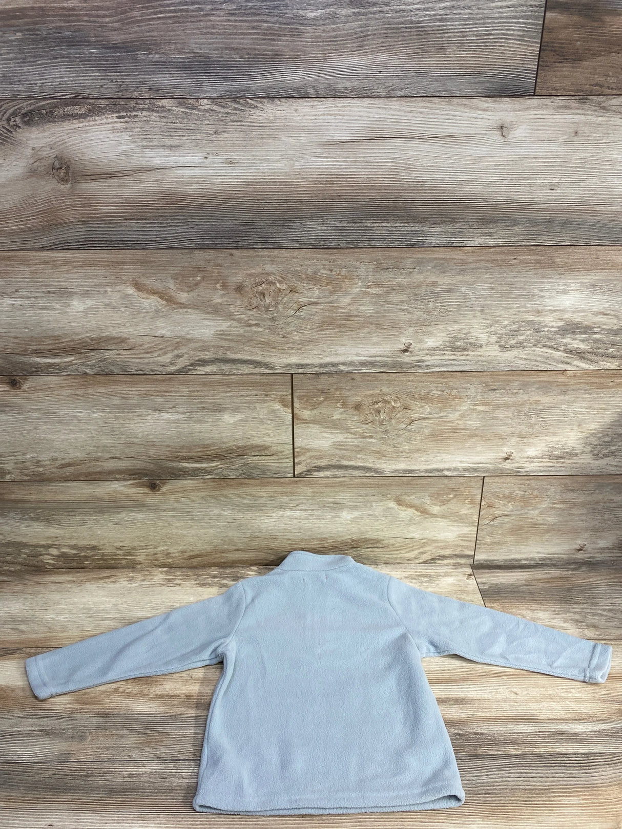 Light blue fleece kids jacket with long sleeves, laid flat on wooden floor background