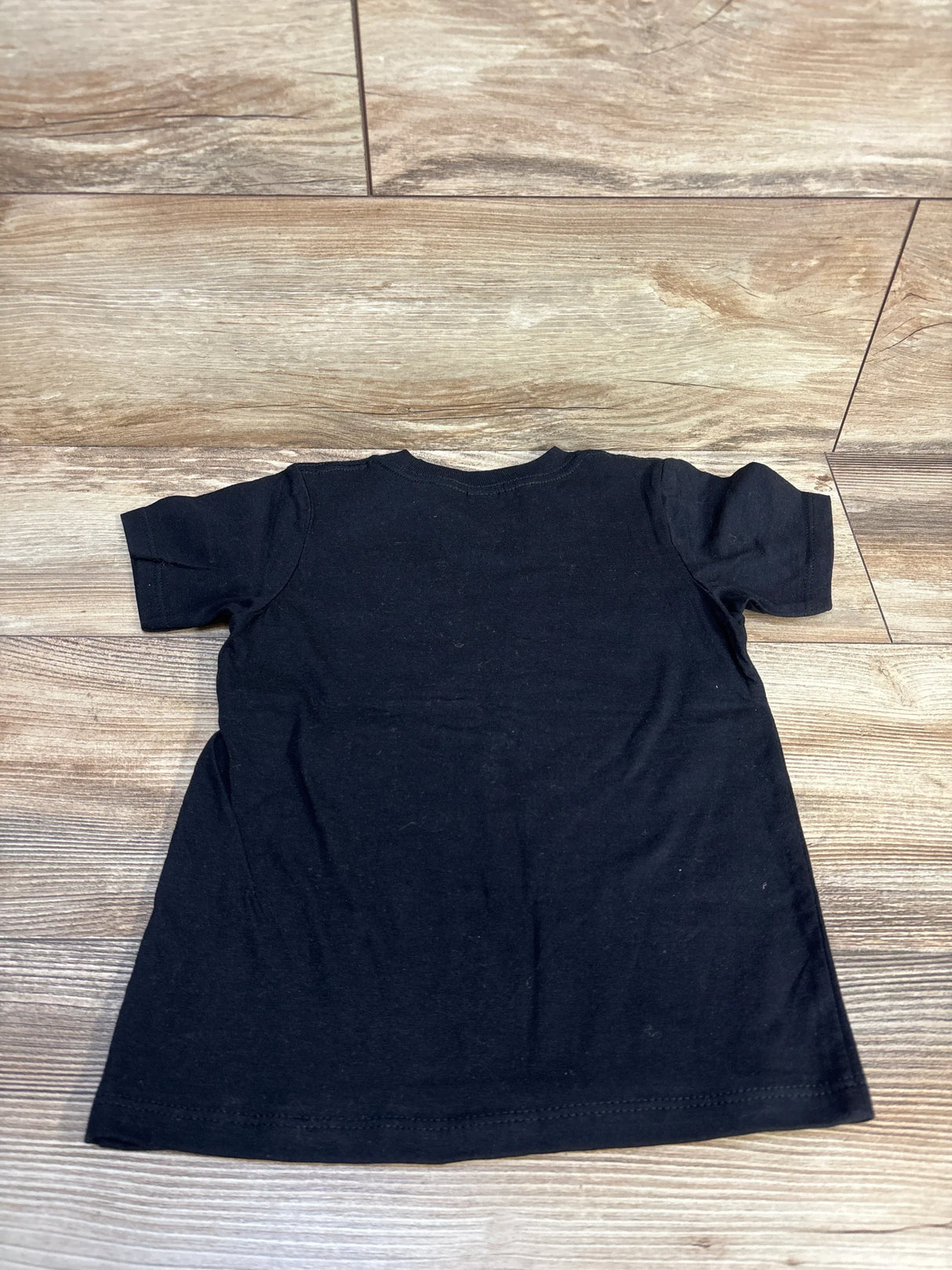 Back view of toddler black Gildan T-shirt (4T) showing plain back and short sleeves, laid flat on wood floor