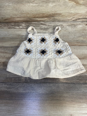 Flat-lay Btween ivory peplum tank top with crochet square yoke and black and tan centers on wood background