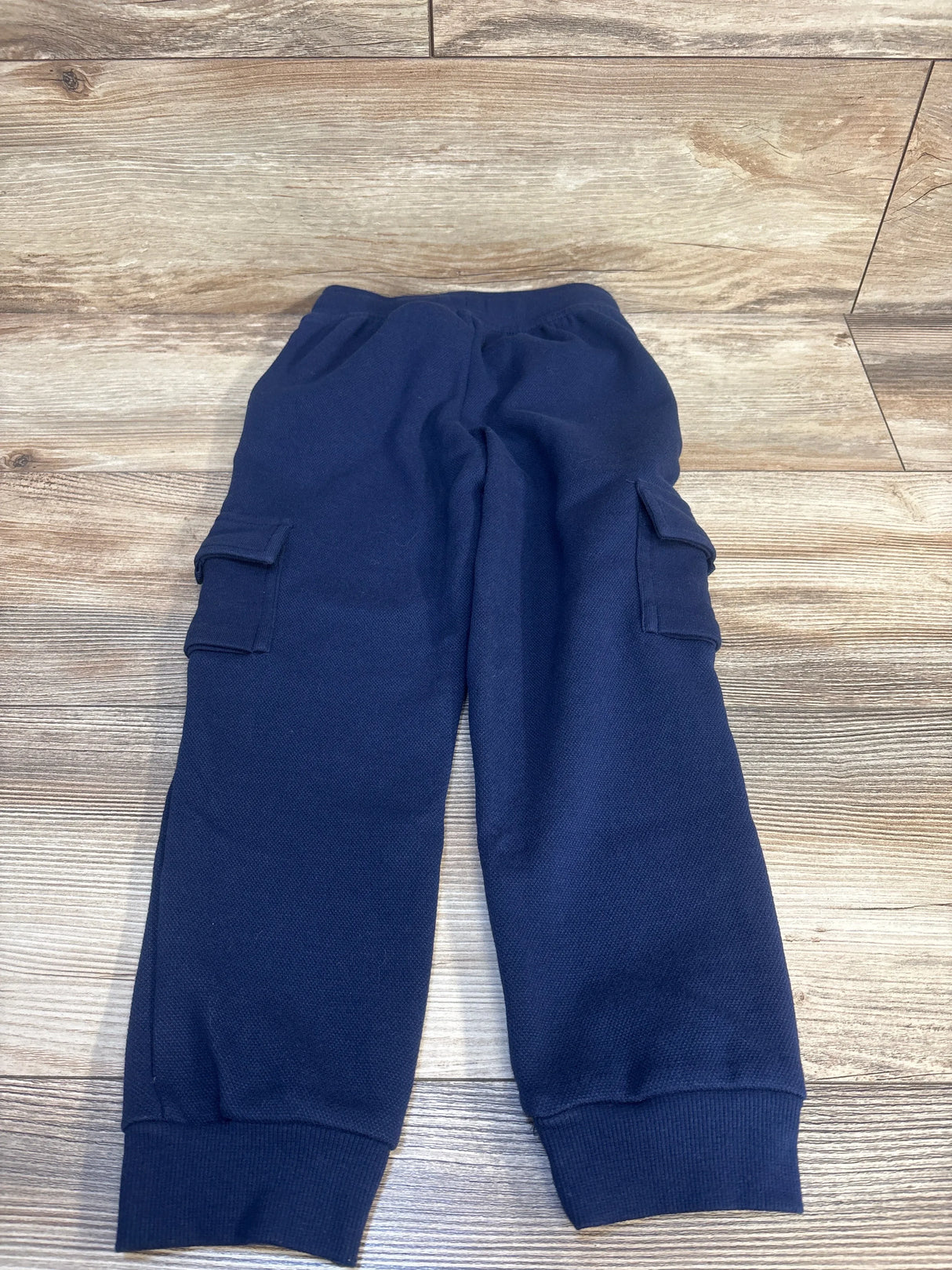 Navy blue kids cargo joggers with elastic waist and side pockets, laid on wood floor