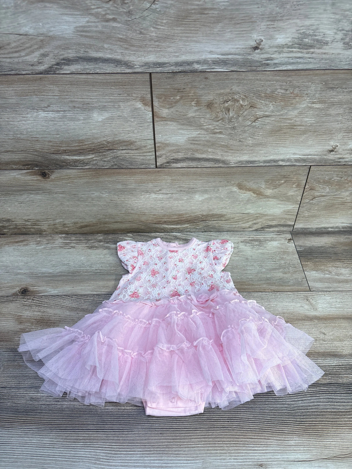 Flat-lay Little Me pink bodysuit dress with floral lace top, flutter sleeves, layered tulle tutu and snap popover on wood