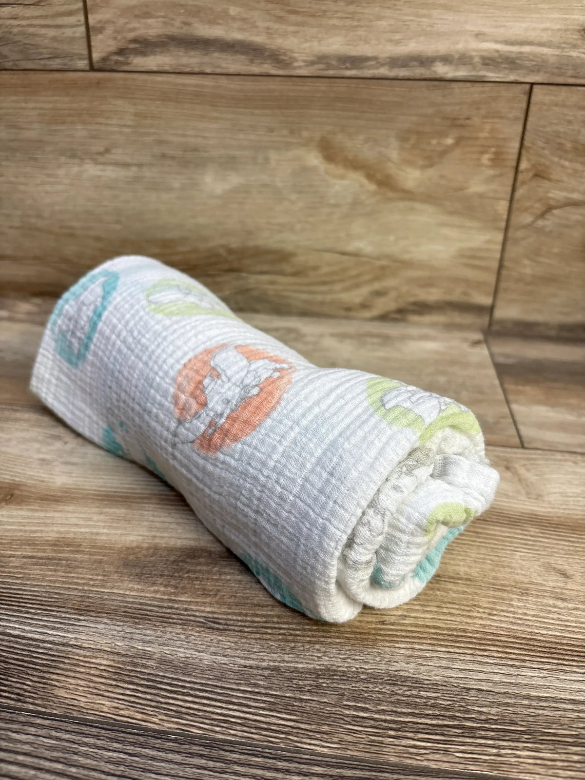 Rolled view of Aden and Anais x Disney Baby muslin swaddle blanket showcasing Dumbo prints on a wood floor