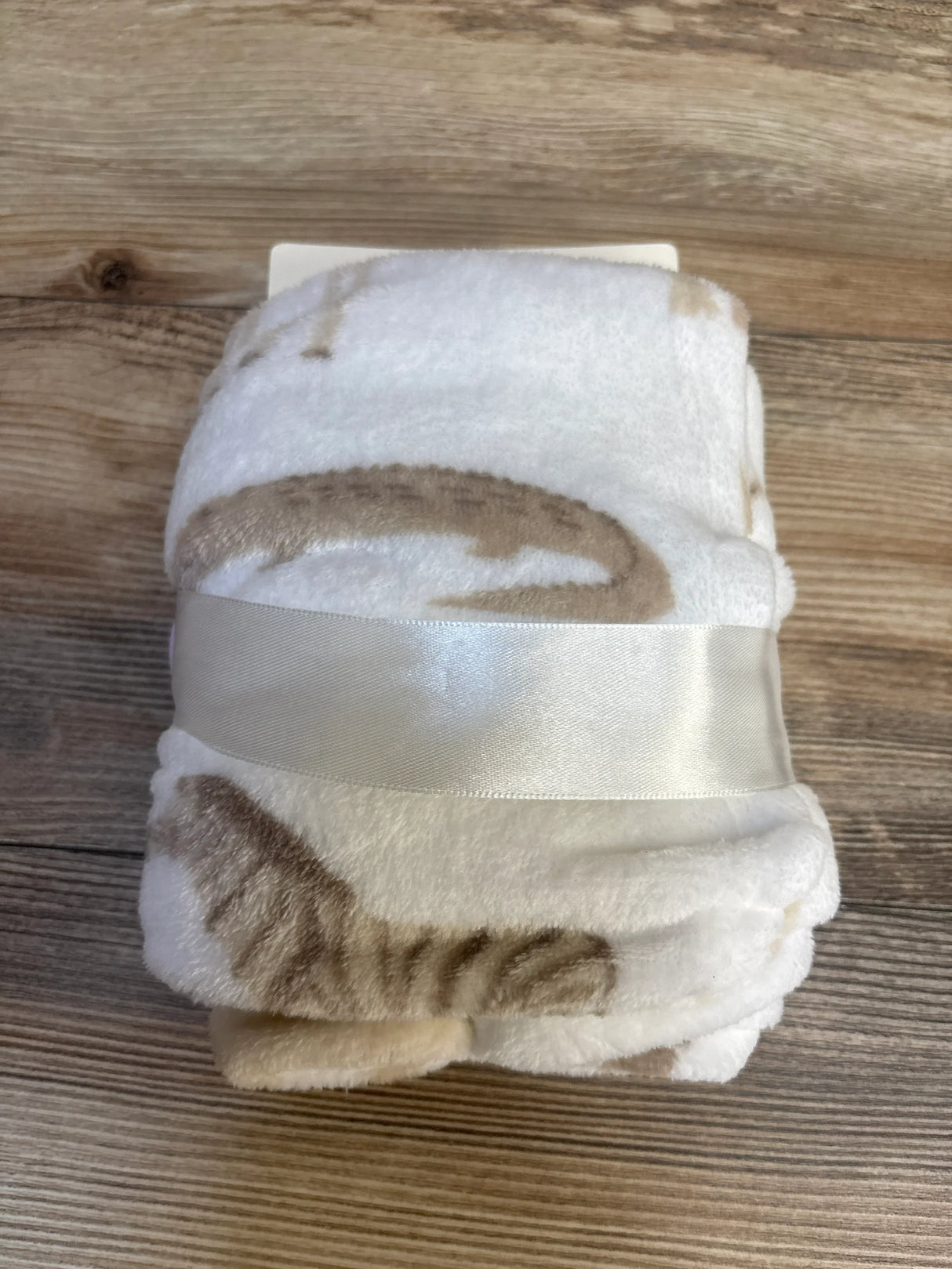 Soft white baby blanket with brown cat print, tied with ribbon, perfect for nursery or baby shower gifts.