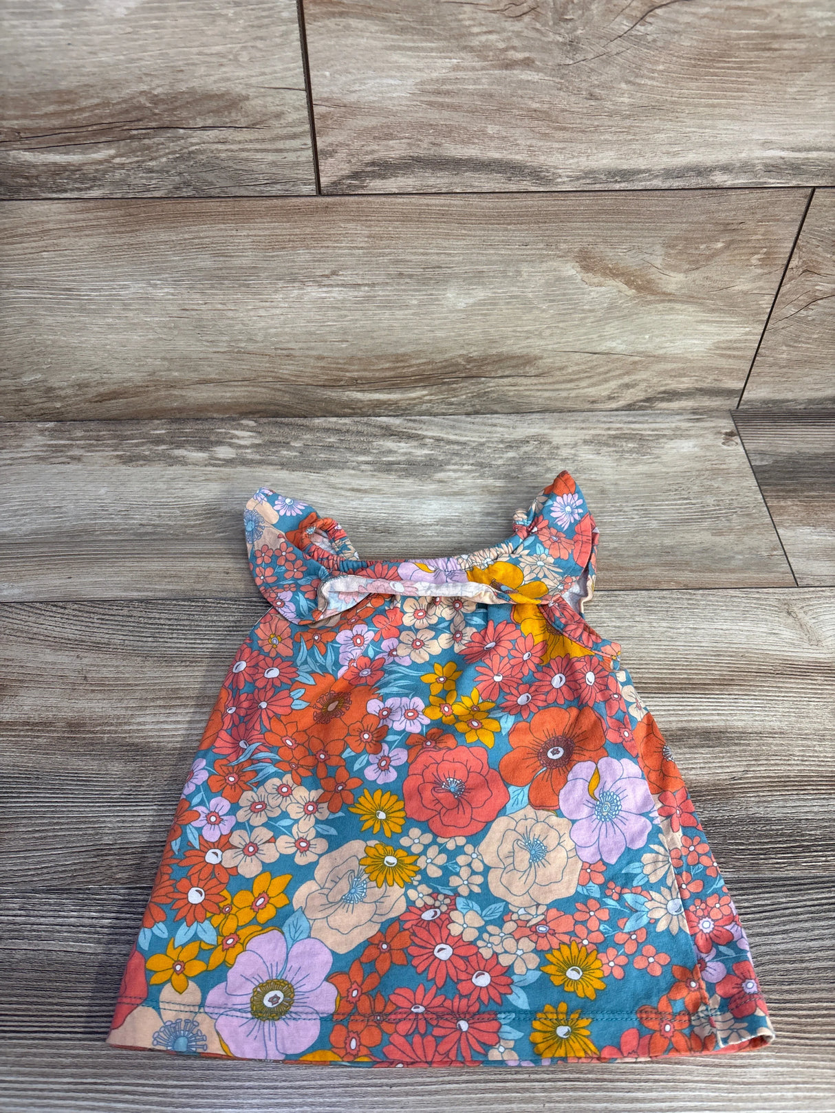 Flat-lay front of girls' blue floral tank top size 2T with ruffle straps on wood background