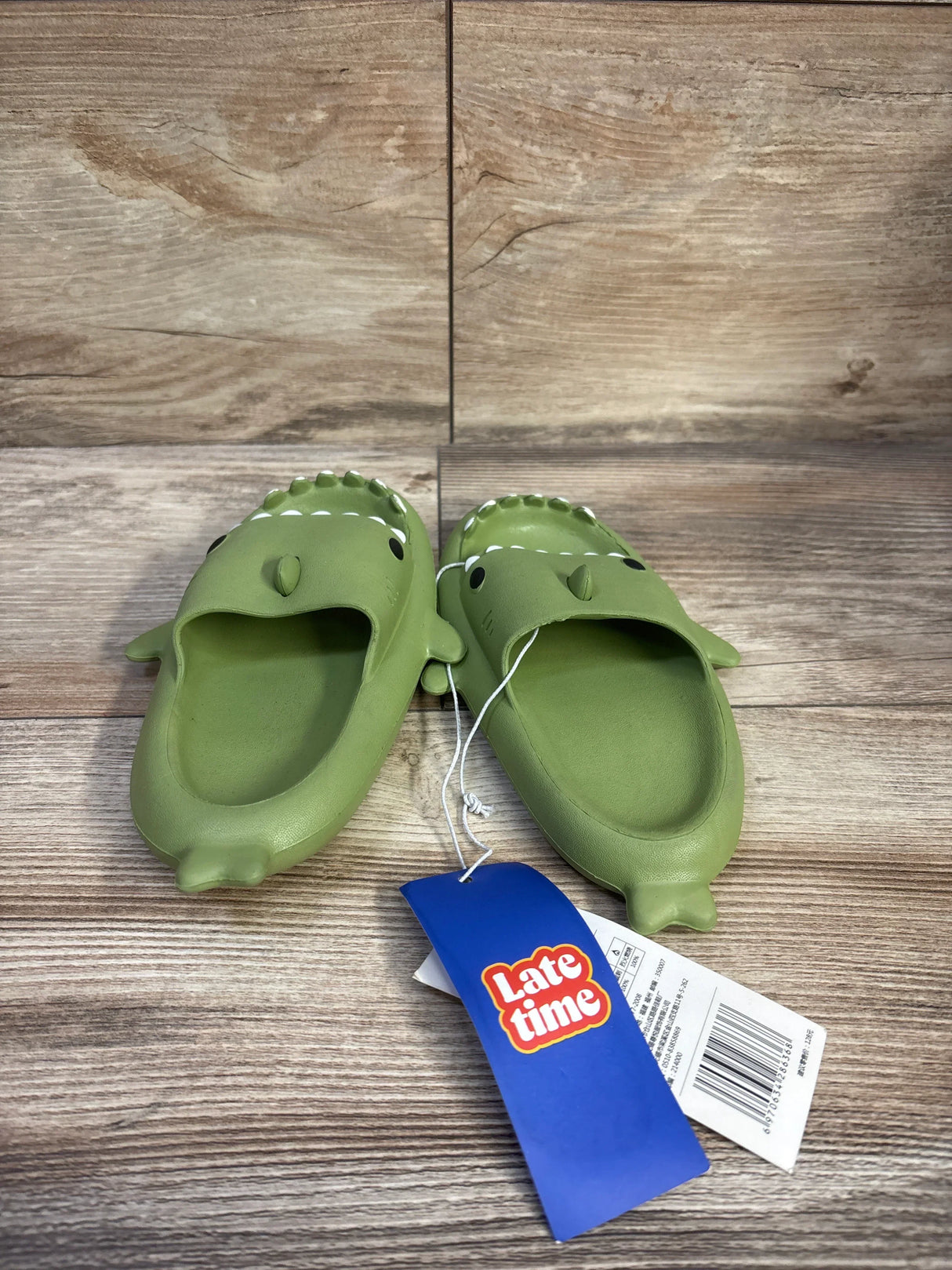 Front view of Crayon Friends green shark toddler slides showing shark face, fins, and textured footbed on wood background