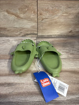 Front view of Crayon Friends green shark toddler slides showing shark face, fins, and textured footbed on wood background