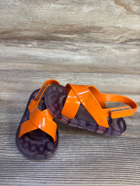 Angled view of Mini Melissa Friendly BB jelly sandals size 8C showing orange crisscross straps, purple translucent soles, and back Velcro strap on wood background