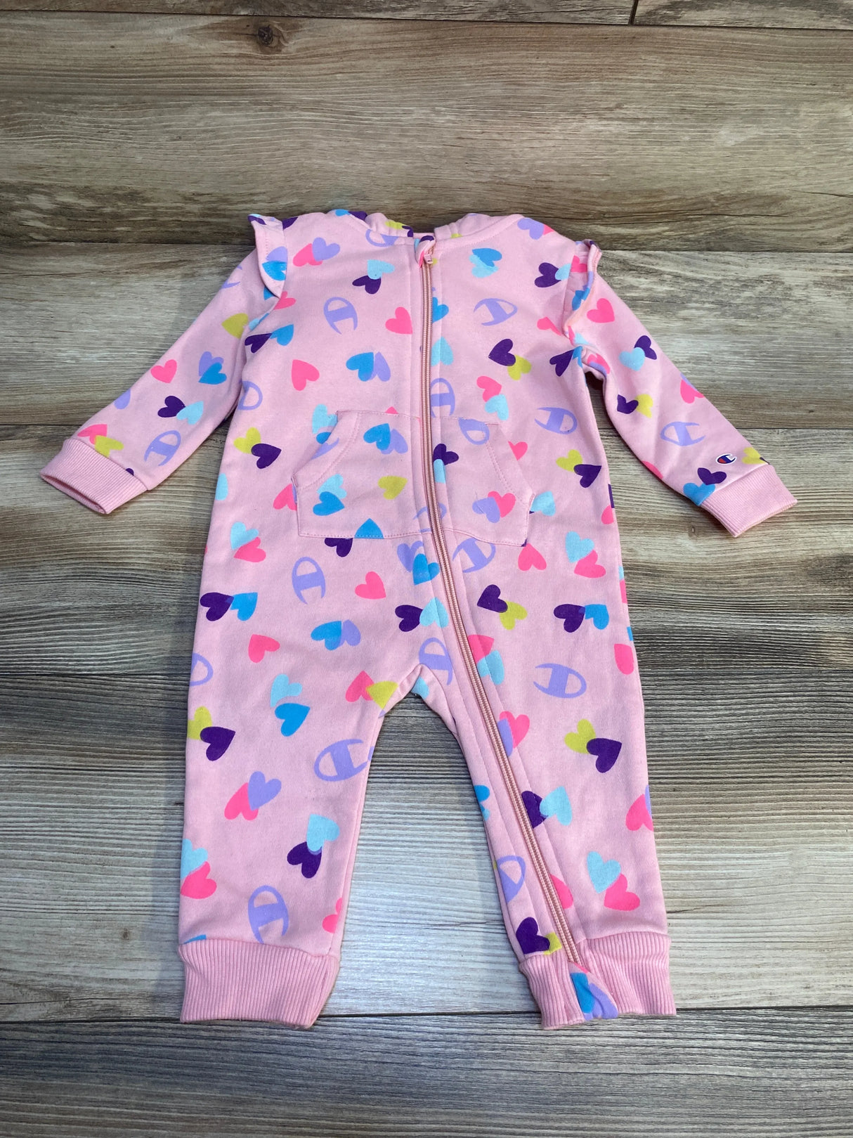 Pink baby sleeper with colorful heart print and zipper, laid flat on wooden floor