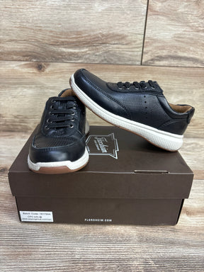 Black kids sneakers with white soles displayed on a shoebox, wooden background