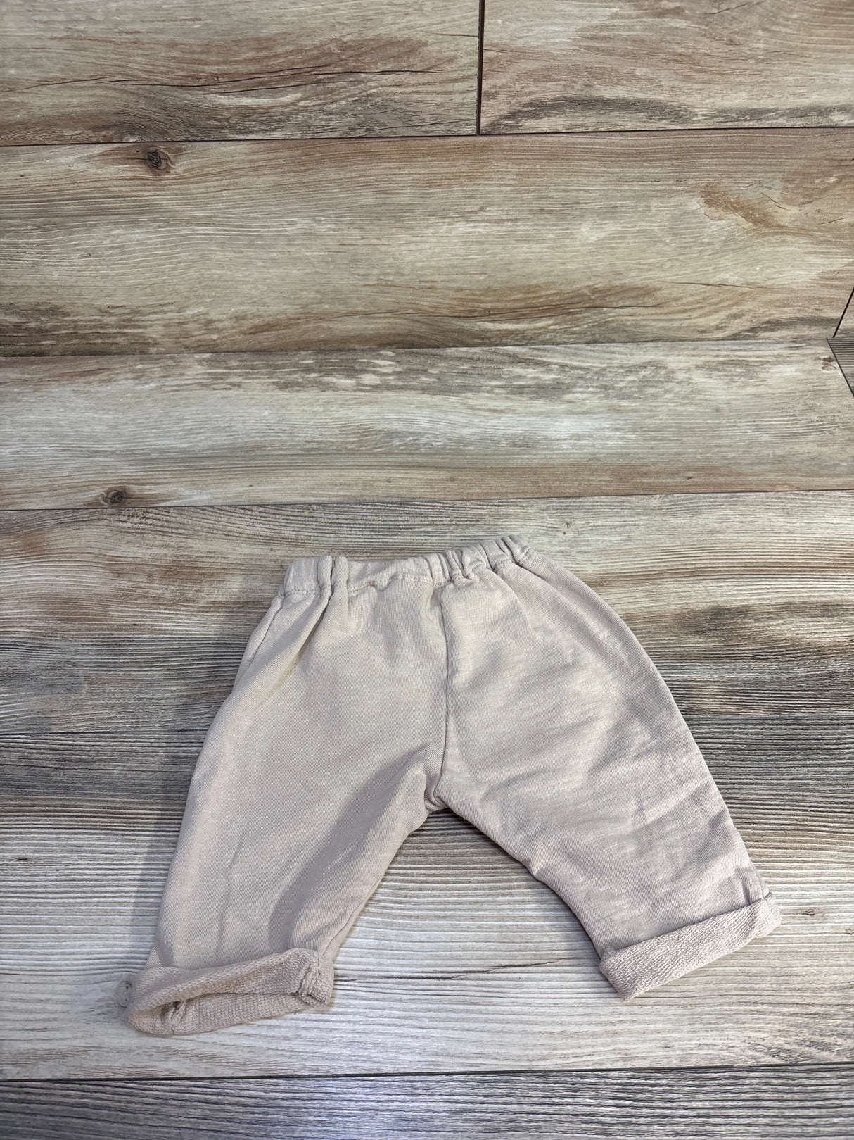 Flat lay of tan H&M baby drawstring joggers showing elastic waistband and rolled cuffs on wood background