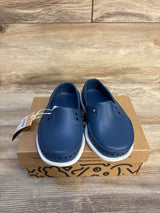 Navy blue slip-on kids shoes with white soles displayed on a shoe box, wood background