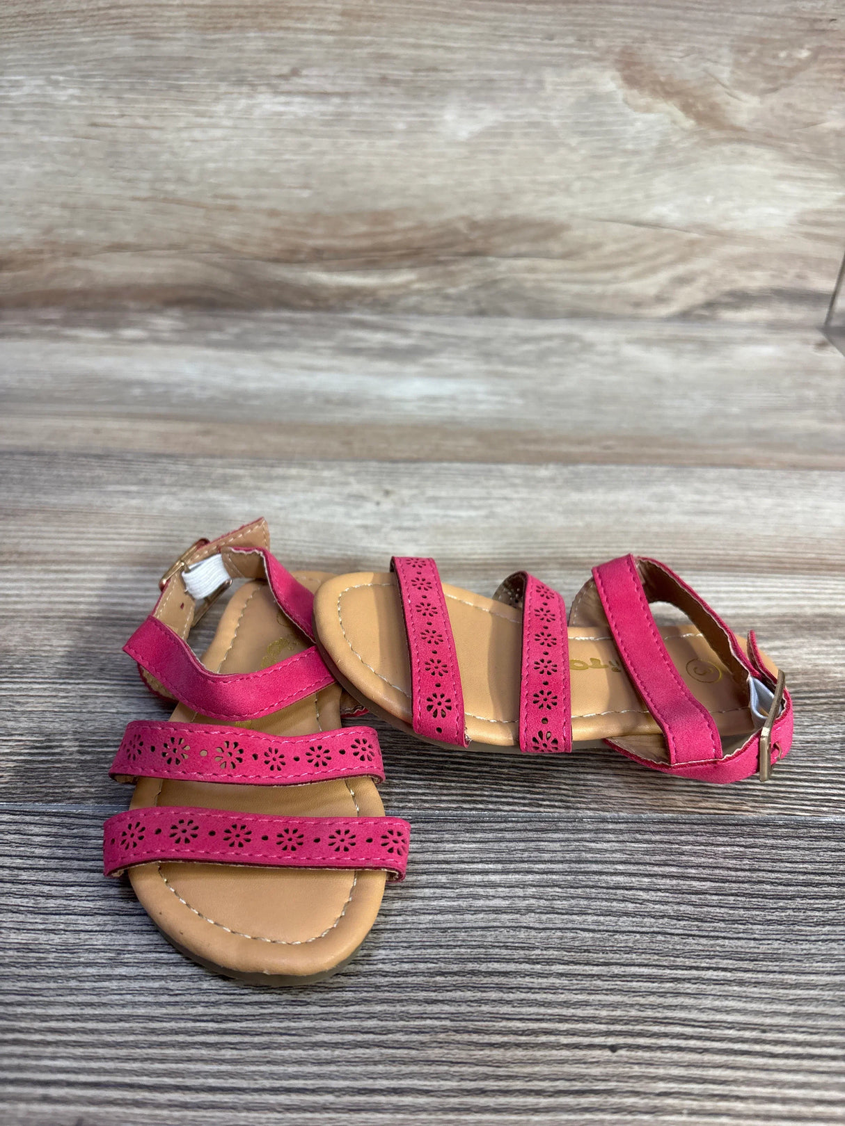 Front view of Ositos slingback sandals, pink size 5C, showing three floral cutout straps and ankle buckle on wood-grain background