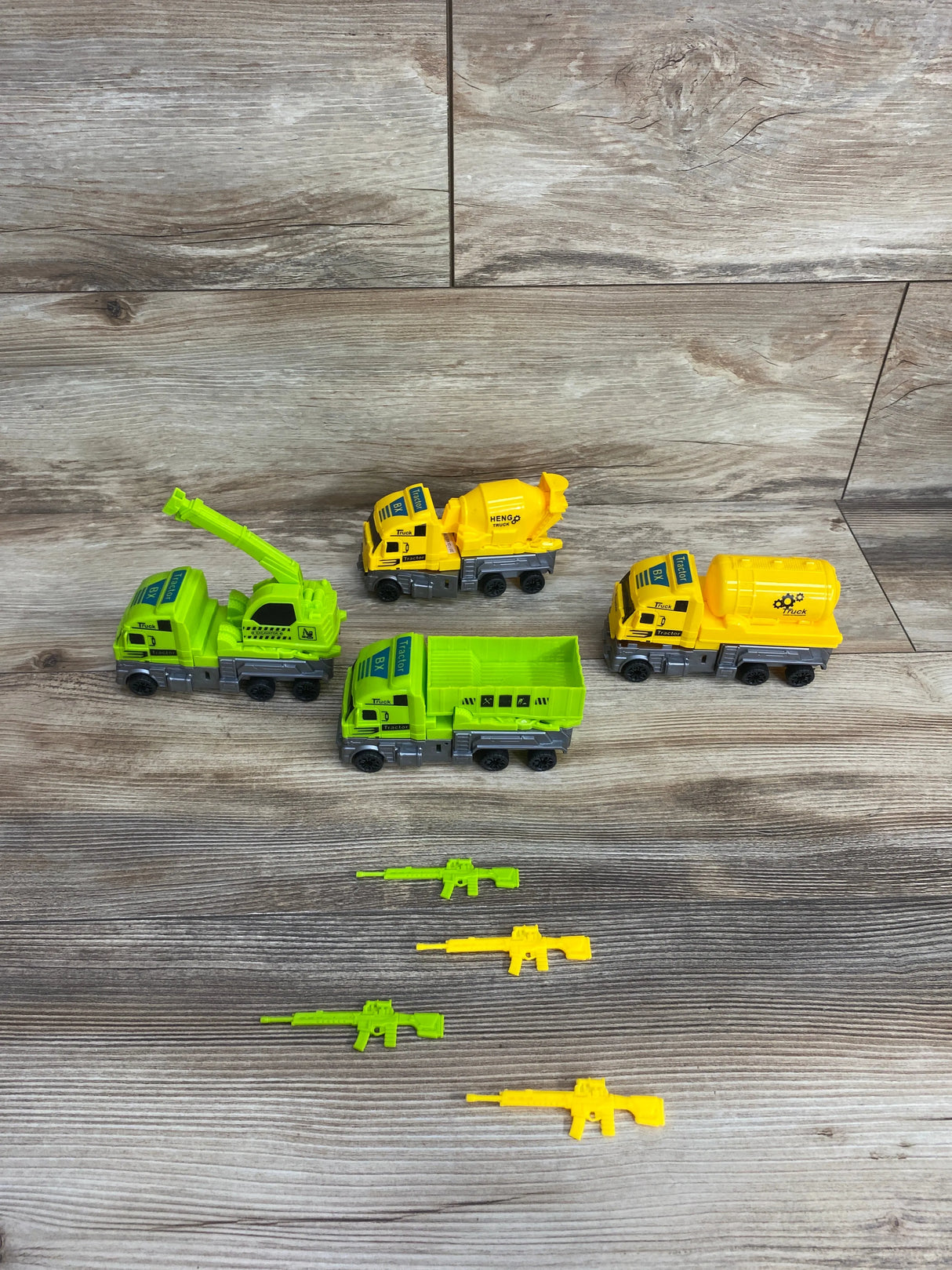 Set of green and yellow toy construction trucks and matching toy rifles on wood floor