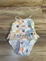 Flat lay of girls Bluey one-piece peplum swimsuit showcasing ruffle waist and halter strap with wood plank background