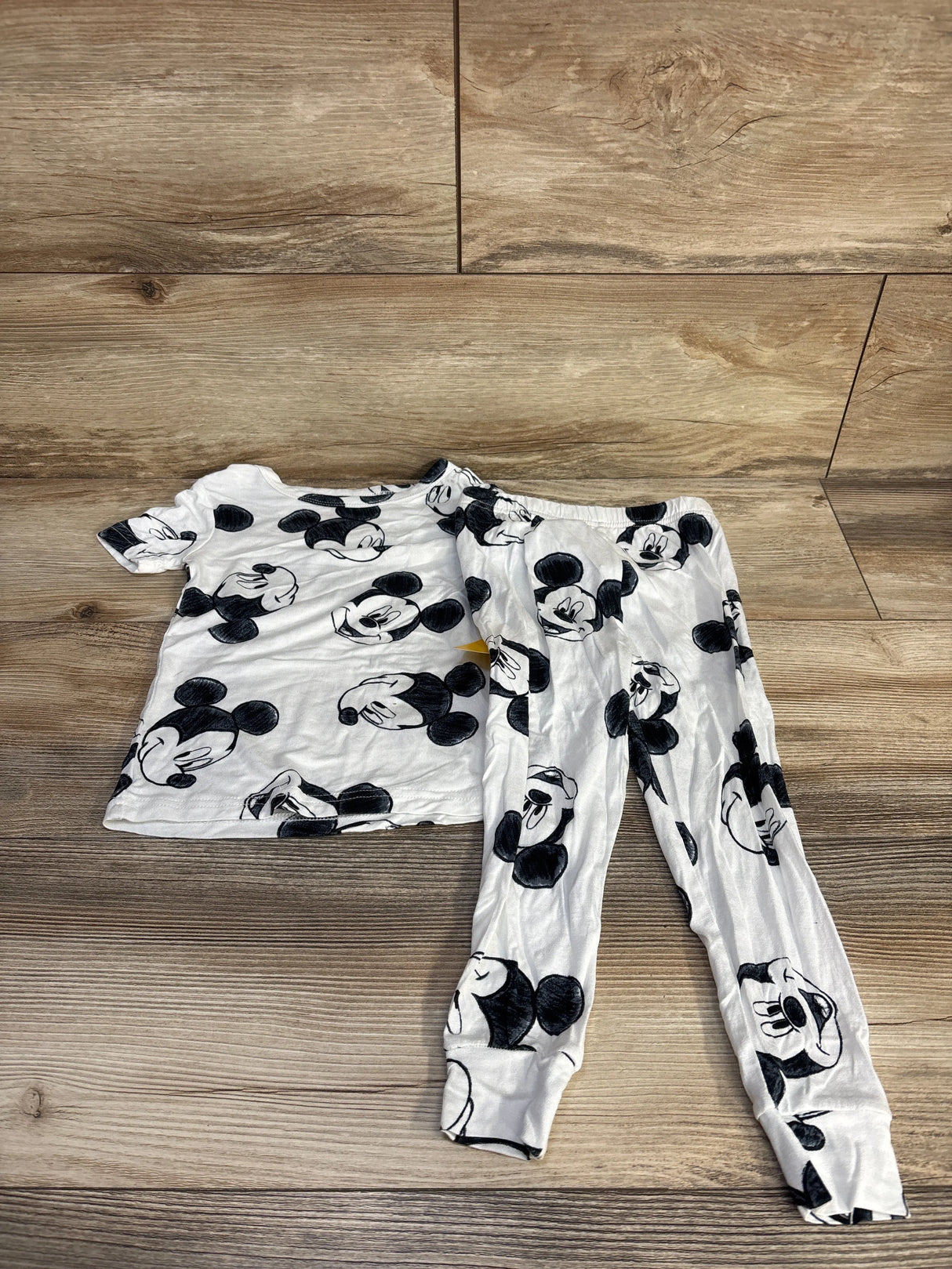 Flat lay of toddler white Disney Mickey 2-piece viscose pajama set showing black Mickey face print on wood floor