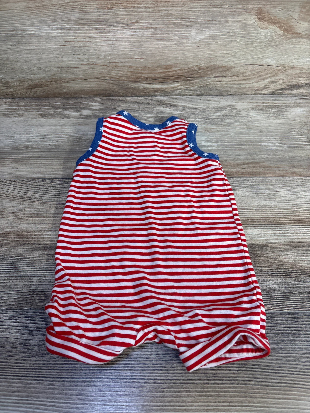 Flat-lay of newborn red-and-white striped sleeveless Henley shortie romper showcasing blue star-trim on a wood background