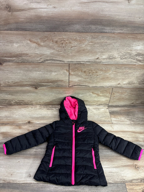 Top view of black Nike hooded puffer jacket, size 2T, showcasing pink lining, zipper, trim, and quilted panels on wood floor