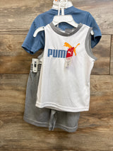 Front view of 3-piece baby Puma set: white tank with blue PUMA text and orange puma logo, blue tee, and gray shorts on wooden background