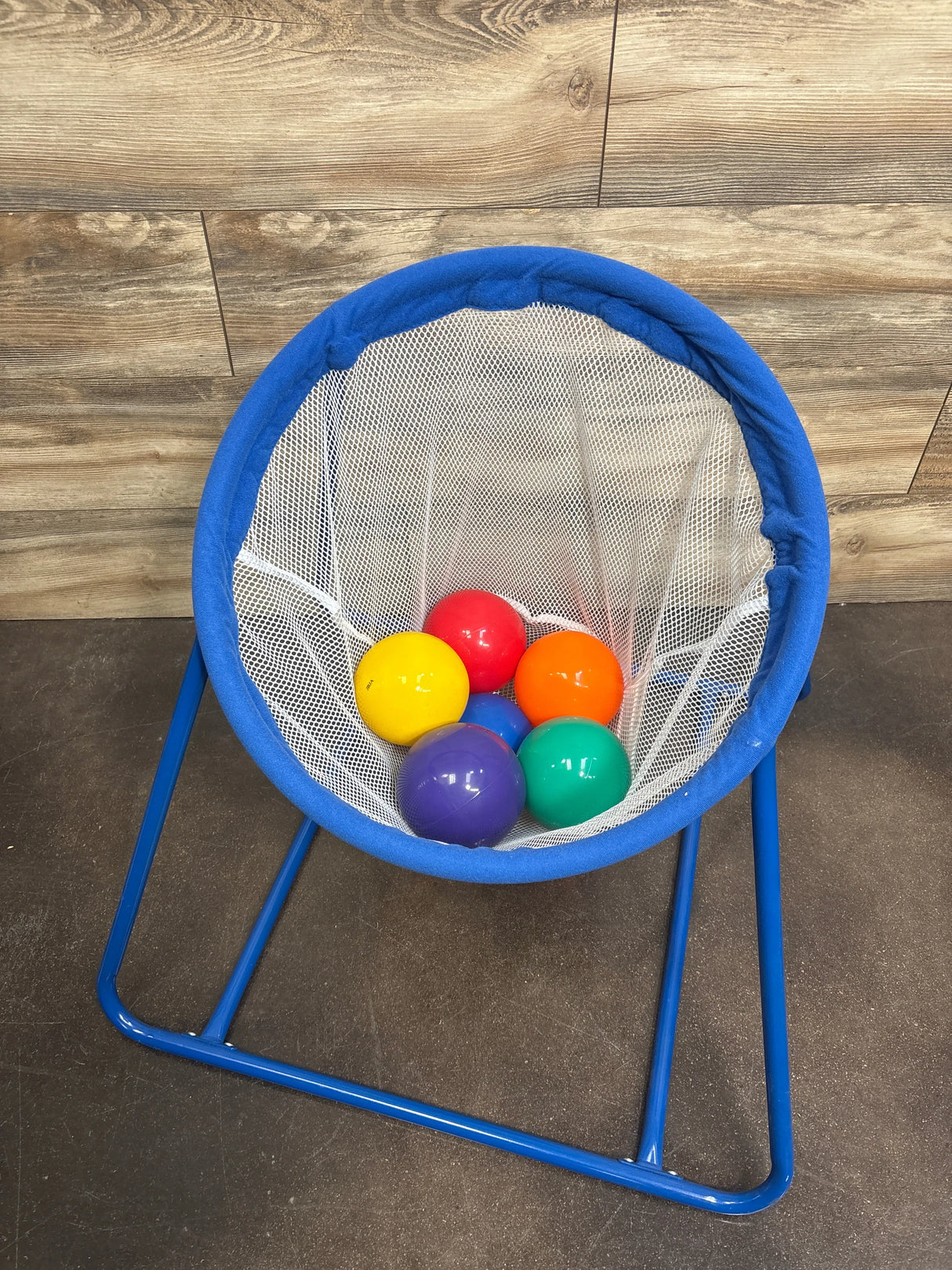 Top-down view of Lakeshore Learning ball toss set showing blue frame and white mesh hoop with six colorful balls on wood floor