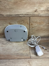 Back of Homedics MyBaby SoundSpa showing battery compartment and DC jack with white AC adapter on wood surface